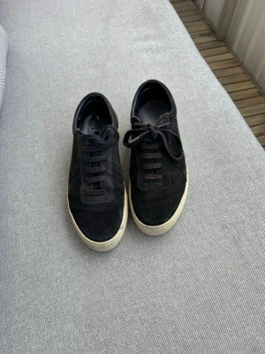 Svarta sneakers från Axel Arigato  - Svarta sneakers från Axel Arigato med klassisk låg profil och tjock vit sula. Skorna är gjorda i mocka och har svarta skosnören. Perfekt för dig som gillar en stilren och enkel look.