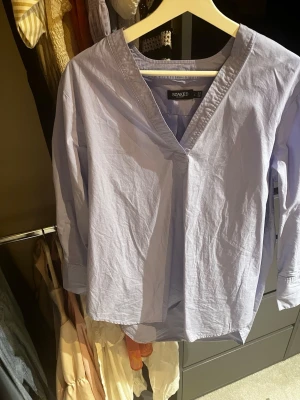 Ljusblå blus från Soaked in Luxury - Stilren ljusblå blus från Soaked in Luxury med v-ringning och avslappnad passform. Blusen har trekvartsärm och är tillverkad i ett lätt bomullsliknande material. Perfekt att matcha med jeans eller kjol för en enkel och snygg look.