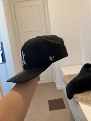 Svart New York Yankees keps från '47 - Säljer en svart keps från '47 med klassisk New York Yankees-logga broderad i vitt framtill. Kepsen har böjd skärm och justerbar passform. Perfekt för dig som vill ha en stilren och sportig look. Pris går o diskutera