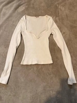 Vit ribbad långärmad topp - Trendig vit ribbad topp med lång ärm och snygg v-ringad skärning. Figurnära passform som framhäver siluetten. Perfekt att styla med jeans eller kjol för en clean look.