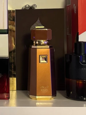 Liquid Brun  - Snygg parfymflaska från Liquid Brun i en lyxig guldbrun färg med geometrisk form och gulddetaljer. Flaskan har en unik, modern design och känns exklusiv med sin metalliska finish och eleganta lock. 