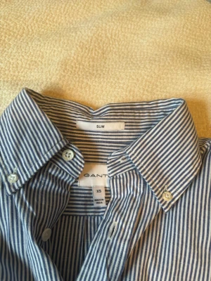 Blårandig skjorta från Gant slim fit - Snygg blårandig skjorta från Gant i slim fit-modell. Skjortan har klassisk krage, knappar framtill och långa ärmar. Tillverkad i bomull för en skön känsla och stilren look. Perfekt för dig som gillar en smalare passform och tidlös design.