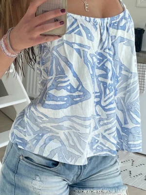Blåvit mönstrad linnetopp - Säljer en luftig blåvit linnetopp med smala axelband och ett abstrakt mönster. Toppen har en avslappnad passform och är perfekt för varma dagar. Materialet känns lätt och svalt mot huden. 