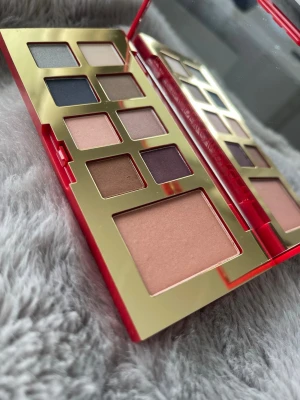 Röd och guld ögonskuggspalett estee Lauder  - Snygg ögonskuggspalett från Estée Lauder i röd och guld förpackning. Innehåller flera nyanser av ögonskuggor i matta och skimrande toner som beige, brun, blå, lila och rosa. Paletten har en stor spegel och elegant design, perfekt för att skapa olika ögonlooks.