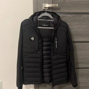 Sail Racing fleece, original pris 3500 kronor. Inga synliga skador Pris 2000 och kan diskuteras - Snygg svart pufferjacka från Sail Racing med huva och dragkedja. Jackan har ett stilrent märke på bröstet och är perfekt för kyligare dagar. Den är långärmad och har en quiltad design som ger extra värme.  Pris kan diskuteras