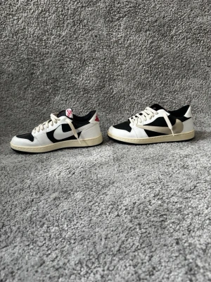 Nike svartvita sneakers låga - Snygga låga sneakers från Nike i svart och vitt med klassisk swoosh på sidan. Skorna har vita snören, svart innerfoder och detaljer i rött på plösen och hälen. Ovandelen är i läder och textil, sulan är ljus och retroinspirerad. Perfekta för en streetwear-look.