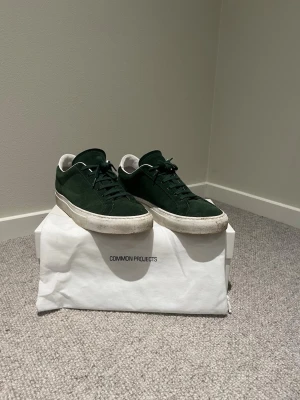 Mörkgröna Common Projects sneakers - Snygga mörkgröna sneakers från Common Projects i mocka med vita detaljer och vit sula. Klassisk låg modell med minimalistisk design och diskret guldprägling på sidan. Perfekta för dig som gillar stilrena och tidlösa skor.