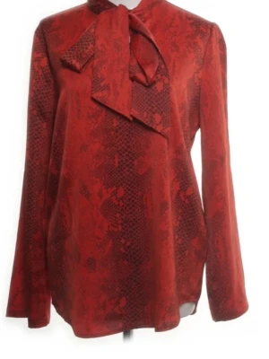 Röd blus med knytband storlek 38 - Snygg röd blus med diskret ormmönster och stort knytband vid halsen. Blusen har lång ärm och rak passform, perfekt för en trendig och elegant look. Materialet ser ut att vara ett mjukt tyg med lätt glans.