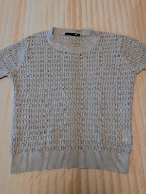 Beige virkad tröja från 157 - Snygg beige virkad tröja från 157 med korta ärmar och rund halsringning. Tröjan har ett luftigt hålmönster och ribbstickade muddar vid hals, ärmslut och nederkant. Perfekt för lager-på-lager och en chill stil.