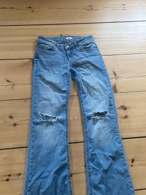 Blå bootcut jeans med hål - Säljer ett par ljusblå bootcut jeans med slitna hål över knäna och broderade detaljer på bakfickorna. 