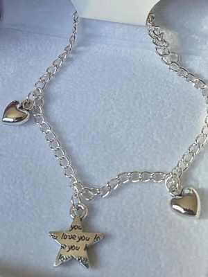 Silverfärgat armband med berlocker - Snyggt silverfärgat armband i rostfritt stål med kedja och tre berlocker: två hjärtan och en stjärna med texten 'I love you'. Perfekt accessoar för att ge din outfit en personlig touch. Armbandet har en enkel och stilren design som passar till många olika stilar. Handgjort.