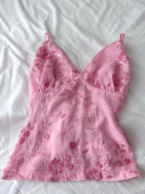 Rosa Y2K topp med pärlor & broderi – Ibiza stil  - Superfin rosa Y2K-topp med blombroderier och små pärldetaljer ✨ Sitter jättefint på med figurnära passform och tunna band.  Ger riktig Ibiza / beach club / sommarkväll-känsla 🌴 Perfekt till semester, festival, utekväll eller middagar i solnedgången. Så snygg med linnebyxor, lågmidjade jeans eller en söt kjol.  • Skick: mycket bra • Storlek: XS–S • Färg: rosa • Stil: Y2K / Ibiza / coquette  #y2k #ibizastil #sommartopp #rosatopp #utekväll #festivaloutfit #beachclub #trendigt #2000tal #pärldetaljer
