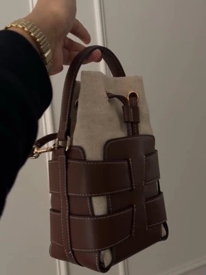 Brun och beige bucket bag i läder -  Säljer en superfin bucket bag från H&M i brunt konstläder med beige tyginsida. Stilren och trendig modell med dragsko och kort handtag - passar både till vardag och finare tillfällen . 💕 Detaljer: • Färg: Brun & beige • Dragsko-stängning  • innerpåse i tyg • Helt ny Hör av dig vid frågor!💕