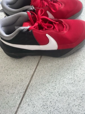 Röda Nike sneakers med vit swoosh - Snygga sneakers från Nike i rött meshmaterial med svart sula och paneler. Skorna har en stor vit swoosh på sidan och grå insida. Klassisk låg modell med röda skosnören och sportig vibe.