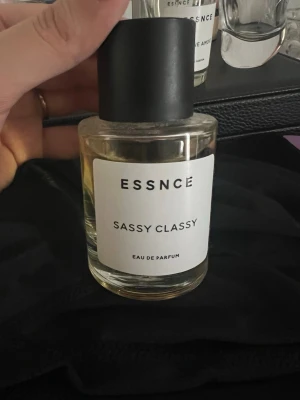 ESSNCE Sassy Classy Eau de Parfum - ESSNCE Sassy Classy Eau de Parfum i en stilren, rund glasflaska med svart lock och vit etikett. Doften kommer i en transparent flaska som ger ett lyxigt och minimalistiskt intryck. Perfekt för dig som gillar moderna och eleganta parfymer. Lyxig doft inspirerad av ysl libre parfymen HELT NY OCH OANVÄND 