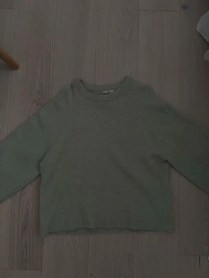 Grön stickad tröja med rund hals - En enkel och stilren grön stickad tröja med rund halsringning och ribbade muddar vid ärmslut och nederkant. Perfekt för lager på lager och passar till det mesta i garderoben.