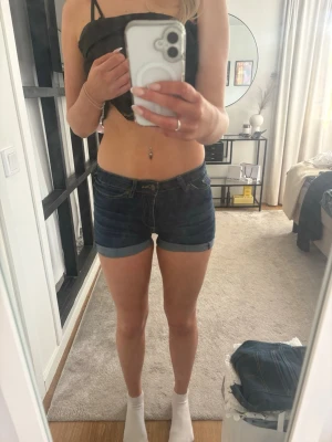 Mörkblå jeansshorts  - Säljer ett par mörkblå jeansshorts med klassisk femficksmodell och uppvikta benslut. Shortsen har normal passform och midja, perfekta för sommaren. Snygga att matcha med crop tops eller linnen!