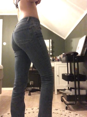 Blå bootcut jeans med låg midja - Säljer ett par blå bootcut jeans med hög midja och klassiska bakfickor. Jeansen har en smal passform över låren och lätt utsvängda ben. Perfekta till sneakers eller boots och ger en snygg siluett.