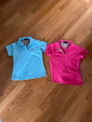 Två pikétröjor från Gant - Säljer två klassiska pikétröjor från Gant, en i ljusblått och en i stark rosa. Båda har korta ärmar, krage och knappar framtill samt randigt tyg på insidan av kragen. Perfekta för en stilren och sportig look.