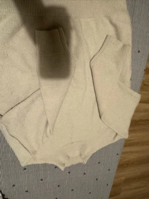 Beige stickad tröja med rund hals - Mysig beige stickad tröja med rund hals och långa ärmar. Tröjan har ribbstickade muddar vid ärmslut och nederkant, vilket ger en klassisk och enkel look. Perfekt för kyliga dagar och lätt att matcha med olika outfits.