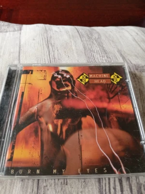Machine Head Burn My Eyes CD - CD-albumet 'Burn My Eyes' från Machine Head i klassiskt plastfodral. Omslaget har en mörk, röd och orange design med bandets logga och albumtitel. Perfekt för dig som gillar metal och vill ha ett samlarobjekt till din musikhylla.