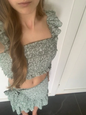 Ljusgrönt blommigt sett med volang  - Säljer en ljusgrön croppad topp med blommigt mönster och volangdetaljer med matchande omlottkjol till. Från märket Shein teen storlek 146. Använd några få gånger säljer för att det är för litet.