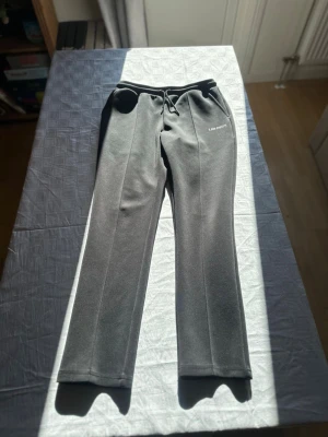 Svarta mjukisbyxor från Les Deux - Snygga svarta mjukisbyxor från Les Deux med raka ben och dragsko i midjan. Byxorna har diskret vit logga på vänster sida och är tillverkade i ett mjukt, stretchigt material som känns riktigt skönt. Perfekta för chill dagar eller när du vill ha en clean look.