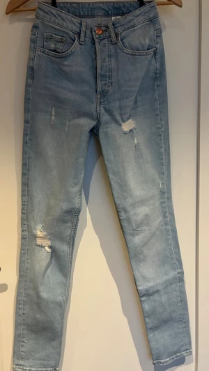 Skinny high waist  - Ett par 5-ficksjeans i ljusblå denim med tvätt och slitna detaljer. Den har hög midja med knappgylf (4 knappar). Storlek: 26 (passar XS/S) Midjemått: 67 cm Insida ben längd: 72 cm  Från rökfritt hem men vi har hundar.