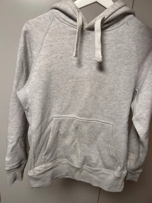 Ljusgrå hoodie med ficka - En stilren ljusgrå hoodie med stor känguruficka framtill och dragsko i huvan. Tillverkad i mjukt bomullsmaterial och har ribbade muddar vid ärmslut och nederkant. Perfekt för en avslappnad och bekväm look.