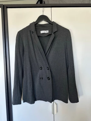 Mörkgrå kavaj storlek xs  - Stilren mörkgrå kavaj med dubbelknäppning och klassisk krage. Tillverkad i mjukt tyg som ger en avslappnad men ändå dressad look. Perfekt till både jeans och kostymbyxor.