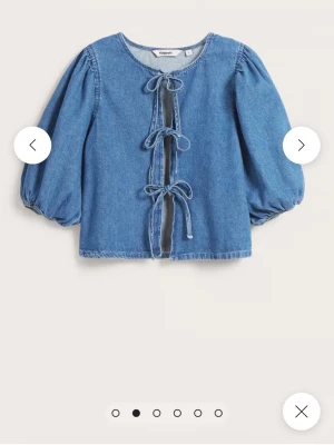 Blå jeansblus med knyt från Kappahl - Säljer en blå jeansblus från Kappahl med tre dekorativa knytband framtill. Blusen har rund halsringning och puffiga trekvartsärmar med resår vid ärmslut. Tillverkad i mjukt denimtyg som ger en avslappnad men trendig look.