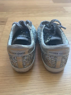 Glittriga Golden Goose sneakers - Säljer ett par riktigt snygga Golden Goose sneakers i lågt modell. Skorna är täckta av silverglitter med detaljer i metallic guld och har leopardmönstrade skosnören. 