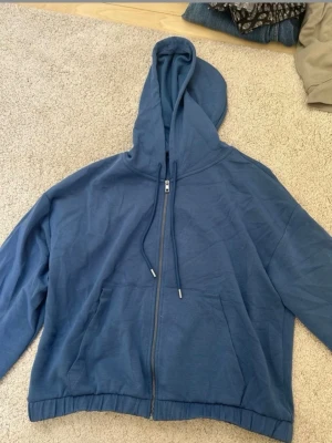 Blå zip hoodie från A New Day - Säljer en blå hoodie från A New Day med dragkedja framtill, justerbar huva med snören och två stora fickor. Tillverkad i mjukt bomullsmaterial som känns skönt mot huden. Perfekt för en avslappnad och chill stil.