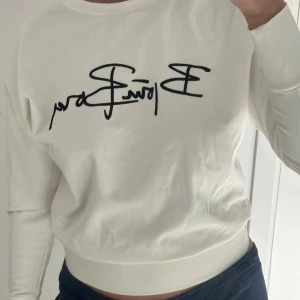 Vit sweatshirt Björn Borg - Vit sweatshirt från Björn Borg med svart broderad logga framtill. Tröjan har rund halsringning, långa ärmar och ribbade muddar vid ärmslut och nederkant. Perfekt för en avslappnad och sportig stil.