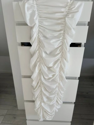 Vit långklänning med rynkade detaljer - Elegant vit långklänning från shein med rynkade detaljer längs hela framsidan som ger en snygg draperad effekt. Klänningen har en smal passform och är perfekt för dig som vill sticka ut med en unik look.