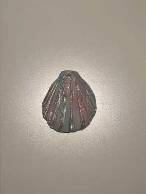 Pastellfärgad snäcka i keramik - Säljer en dekorativ snäcka i keramik med skimrande pastellfärger i rosa, blått och lila med ett hål. Snäckan har räfflad yta och glänsande finish, perfekt som prydnad eller som berlock på smycke.
