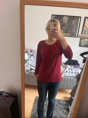 Vinröd blus med rund hals - Säljer en vinröd blus med rundad halsringning och veckdetaljer framtill. Blusen har trekvartsärm och en rak, avslappnad passform. Perfekt att matcha med jeans eller kjol för en snygg look. Helt ny
