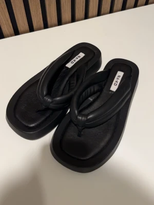 Svarta platåsandaler från NA-KD - Chunky svarta sandaler från NA-KD med breda, vadderade remmar och fyrkantig tå. Nypris 549kr.