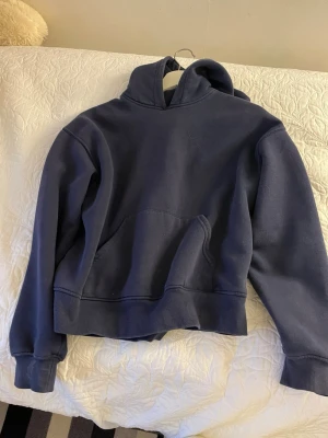 Mörkblå hoodie med huva - En enkel och stilren mörkblå hoodie med huva och stor magficka. Hoodien har ribbade muddar vid ärmslut och nederkant. Perfekt för en avslappnad och casual look. Tillverkad i mjukt sweatshirtmaterial.