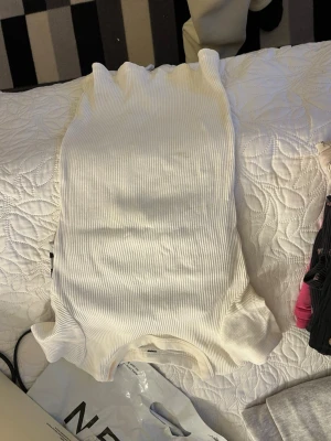 Vit ribbad ärmlös topp - Snygg vit ribbad topp med hög hals och ärmlös design. Perfekt att styla till jeans eller kjol för en clean och fräsch look. Stretchigt material som sitter bekvämt och följer kroppen.