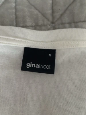 Vit v-ringad långärmad topp Gina Tricot - Klassisk vit långärmad topp från Gina Tricot med v-ringning. Tillverkad i mjukt och stretchigt material som sitter snyggt mot kroppen. Perfekt att styla med jeans eller kjol för en clean look.