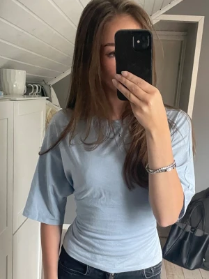 Ljusblå t-shirt med knyt i sidan - Snygg ljusblå t-shirt med knytning i ryggen från Nelly. Knappt använd så super fint skick.