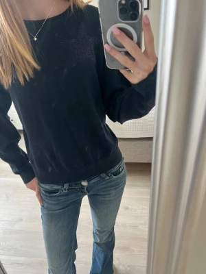 Mörkblå tröja med stjärndetaljer - Säljer en mörkblå tröja med subtila stjärndetaljer på bröstet och sidan. Tröjan har rund halsringning, långa ärmar och ribbade muddar. Perfekt för dig som gillar en enkel men ändå unik stil. Den är lite större i storlek 