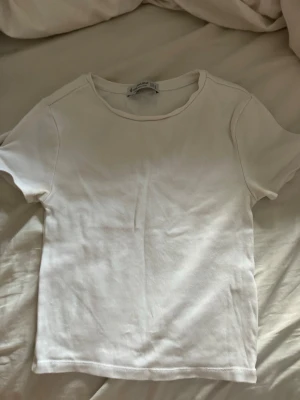 Vit t-shirt från Stradivarius - Klassisk vit t-shirt från Stradivarius i mjuk bomull. Enkel design med rund halsringning och korta ärmar, perfekt till alla typer av outfits. Snygg och stilren basic som alltid funkar.