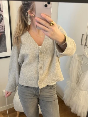 Beige stickad kofta med knappar - Mysig beige kofta med v-ringning och tre stora knappar framtill. 