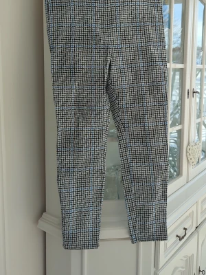 Rutiga kostymbyxor i svart och vitt - Snygga kostymbyxor med svartvitt rutmönster och diskreta blå detaljer. Byxorna  är tillverkade i ett strechigt material som ger en dressad look. Provade annars nya. 