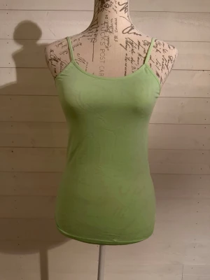 Ljusgrön linnetopp med smala band - Snygg ljusgrön linnetopp med smala axelband och figurnära passform. Perfekt till sommaren och enkel att matcha med olika stilar. Tillverkad i mjuk bomull för en bekväm känsla.