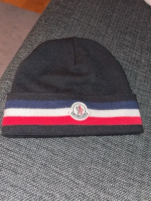 Svart Moncler mössa med ränder - Säljer min Moncler mössa då jag har köpt en Cp company och ej använder mössan längre köpt för 1 månad sedan använd 1-2 gånger 