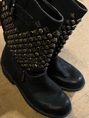 Svarta boots med nitar och spänne - Svarta boots med grov sula, dekorerade med massor av silverfärgade nitar och ett spänne vid ankeln. Aldrig använts, haft den i cirka 10 år utan användning. 