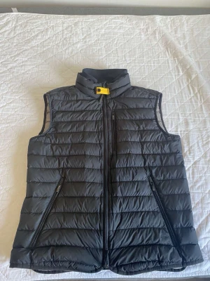 Svart dunväst från Parajumpers - Snygg svart dunväst från Parajumpers med gul detalj vid kragen och två dragkedjeförsedda fickor framtill. Västen har en quiltad design och hög krage, perfekt för lager på lager och streetstyle. Klassisk och stilren look som funkar till det mesta.